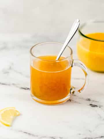 close up side view of cling peach medicine ball in glass mug with spoon by sliced lemon and peach puree