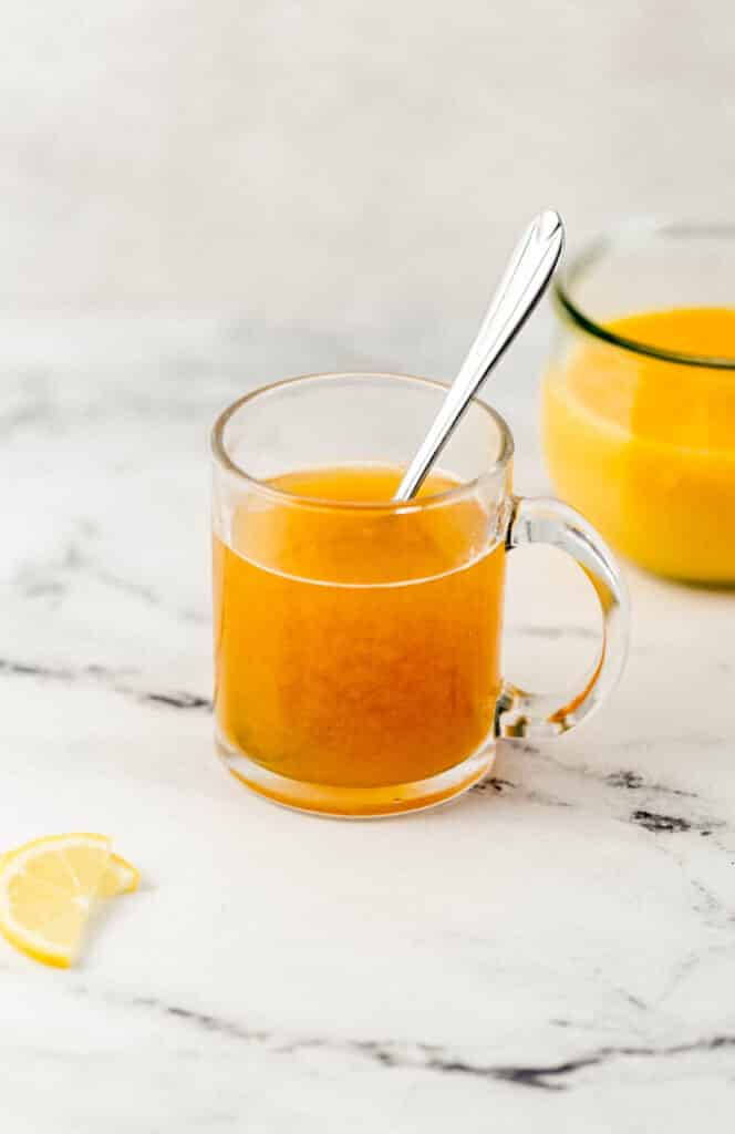 close up side view of cling peach medicine ball tea in glass mug with spoon with lemon spices and separate container of peach puree