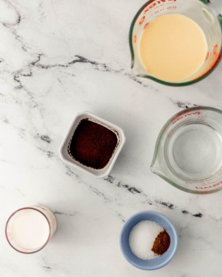 Overhead view of ingredients needed to make latte in separate containers on marble surface.