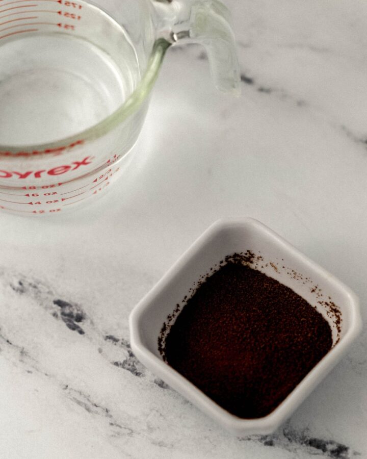 Close up view of water in a measuring cup and a small bowl of espresso powder.