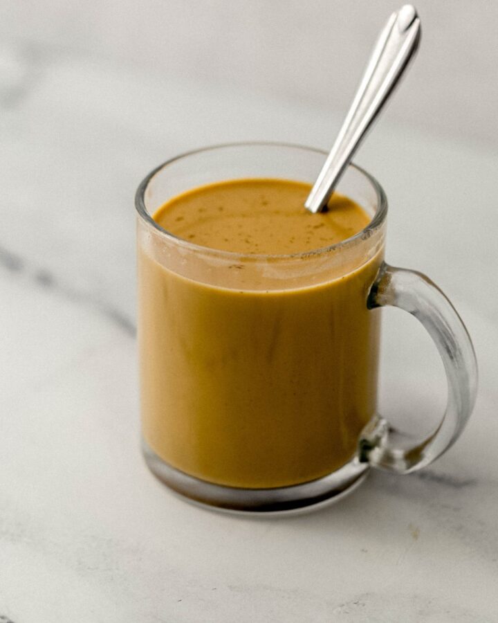 Close up side view of latte in glass mug with spoon in it.