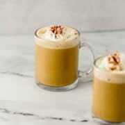 Side view of two finished lattes in glass mugs on marble surface.