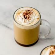 Close up view of finished eggnog latte in glass mug topped with whipped cream.