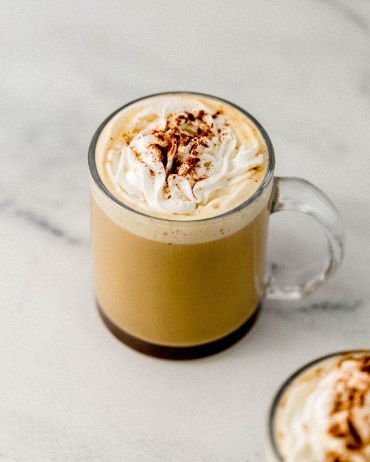 Close up view of finished eggnog latte in glass mug on marble surface.