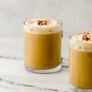 Finished eggnog latte in glass mug on marble surface.
