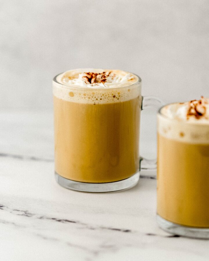 Close up side view of finished latte topped with whipped cream in two glass mugs.