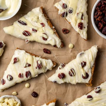 overhead view homemade cranberry bliss bars on brown paper with dried cranberries and melted white chocolate