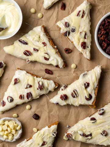 overhead view homemade cranberry bliss bars on brown paper with dried cranberries and melted white chocolate