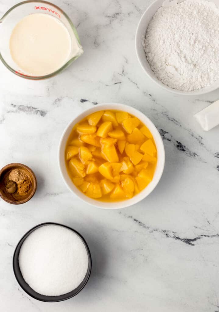 ingredients needed to make easy peach cobbler in separate containers on marble surface 