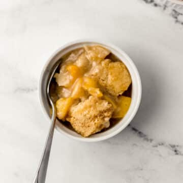 serving of peach cobbler in small white bowl with spoon in it