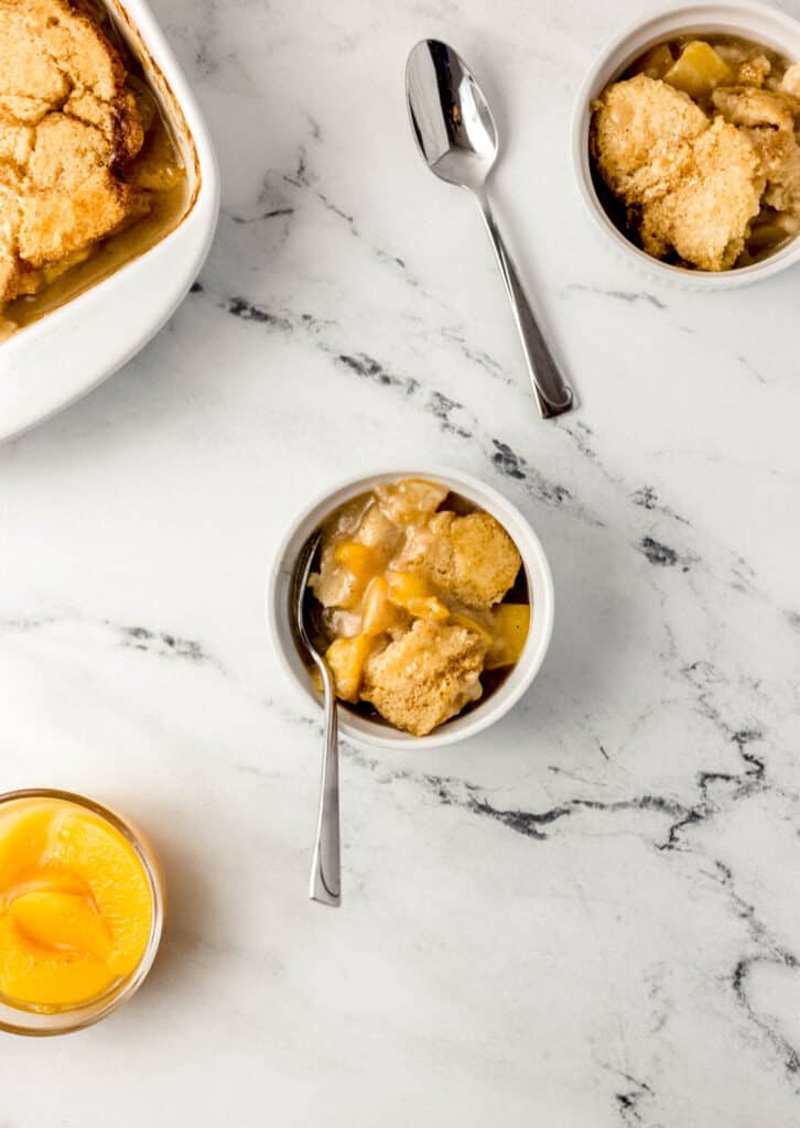 overhead view peach cobbler in small white bowls with baking pan and spoons