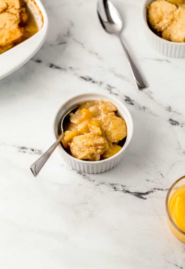 close up side view peach cobbler in small white bowl with spoon