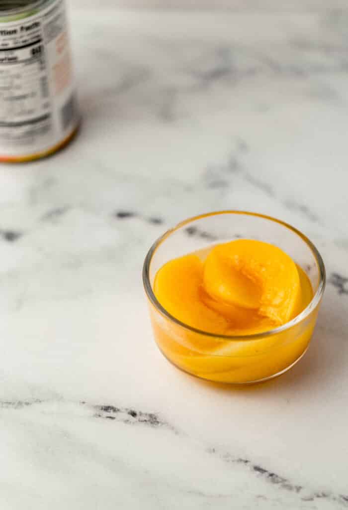 sliced peaches in small glass bowl with can in the background