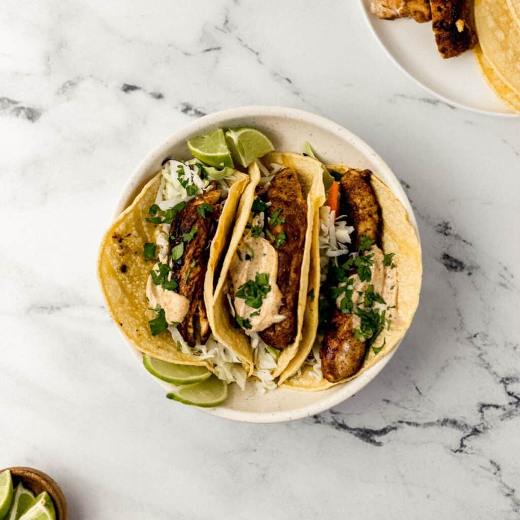 overhead view three jerk chicken taco in white bowl with other bowls of ingredients around it