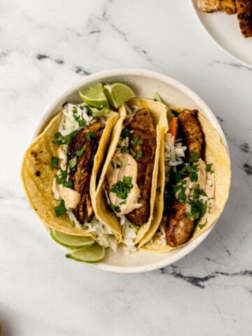 overhead view three jerk chicken taco in white bowl with other bowls of ingredients around it