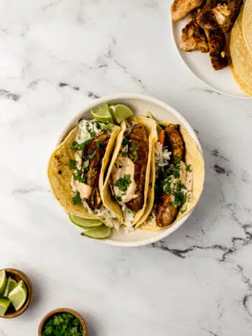 overhead view three jerk chicken taco in white bowl with other bowls of ingredients around it