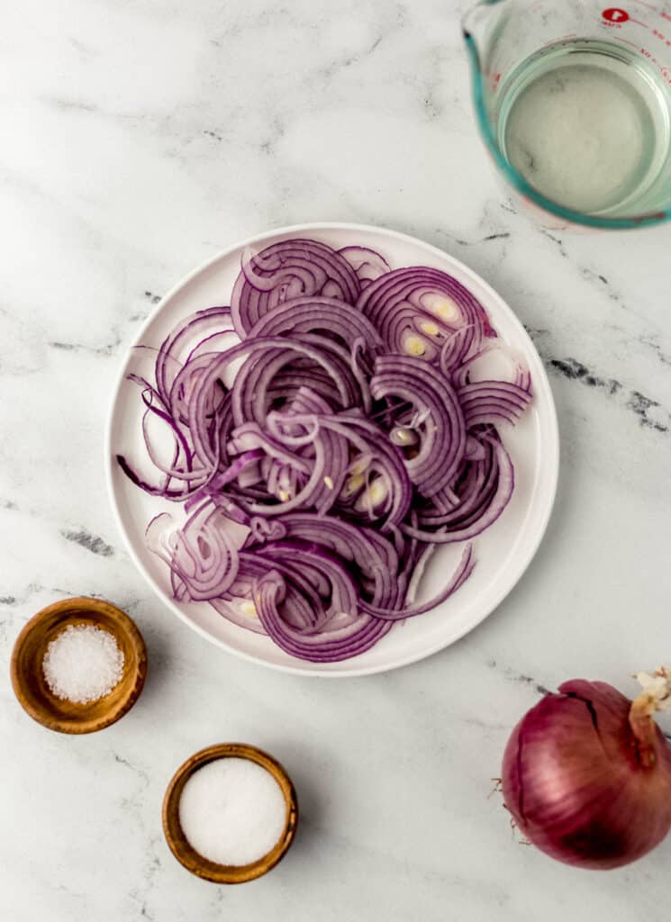 overhead view of ingredients needed to make quick pickled red onions in separate containers on marble surface