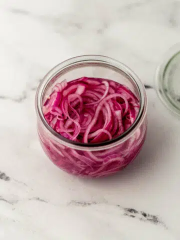overhead view quick pickled red onions in glass jar on marble surface