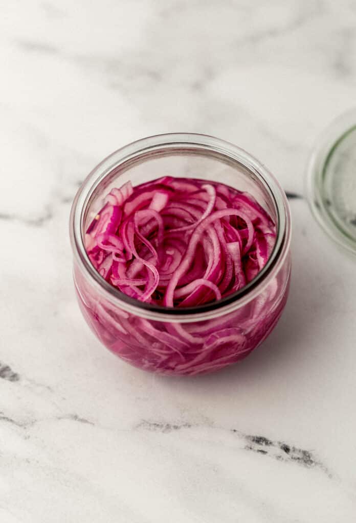 overhead view of finished quick pickled red onions in jar on marble surface