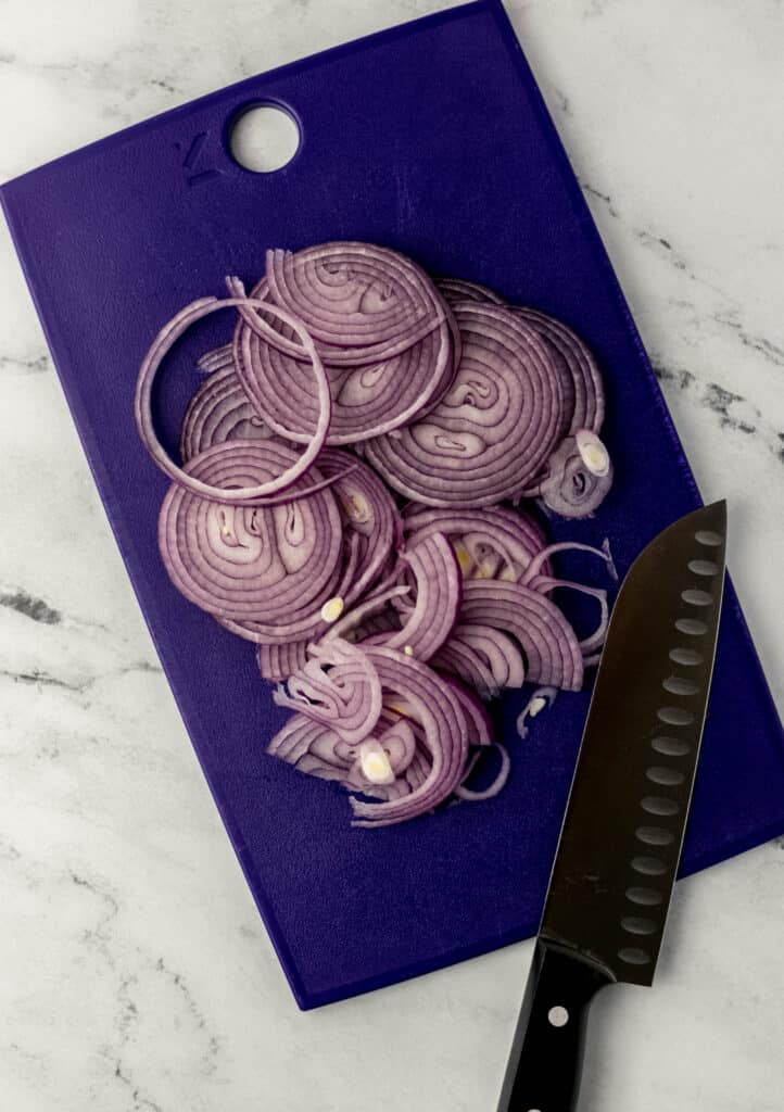 thinly sliced red onion on blue cutting board with knife 