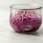 close up side view of quick pickled red onions in wide mouth jar