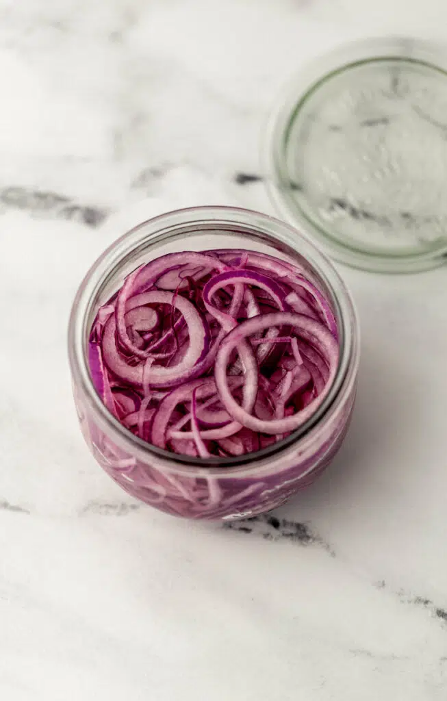 overhead view of prepared quick pickled red onions in wide mouth weck jar beside the lid