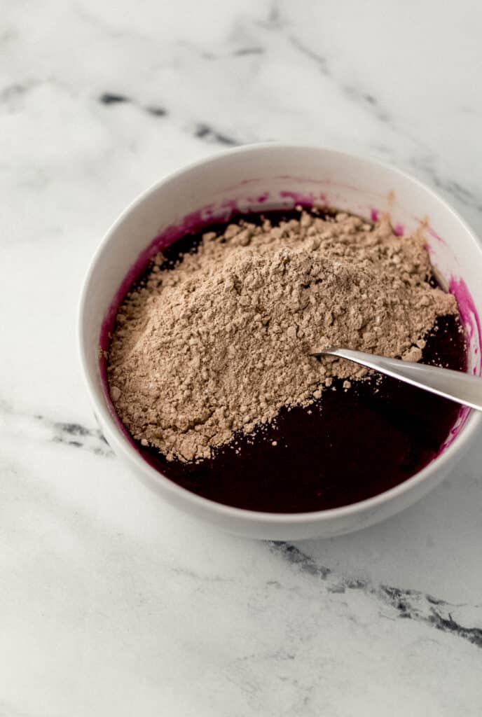 wet and dry red velvet cupcake ingredients combined together in white bowl with spoon