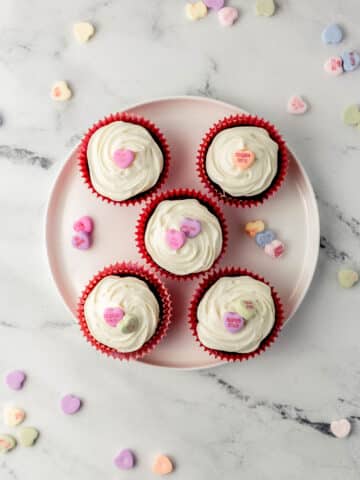 overhead view small batch red velvet cupcakes on white plate topped with candy hearts