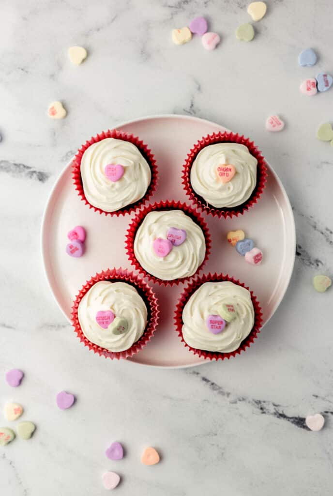 overhead view finished small batch red velvet cupcakes on white plate covered with candy hearts