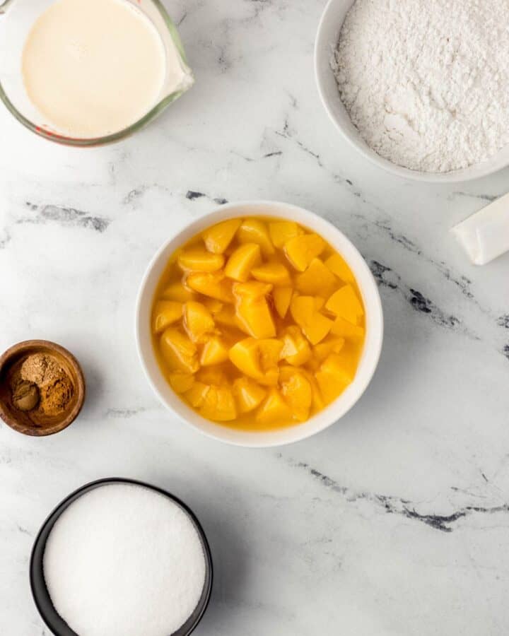 Overhead view of ingredients needed to make peach cobbler in separate bowls. 