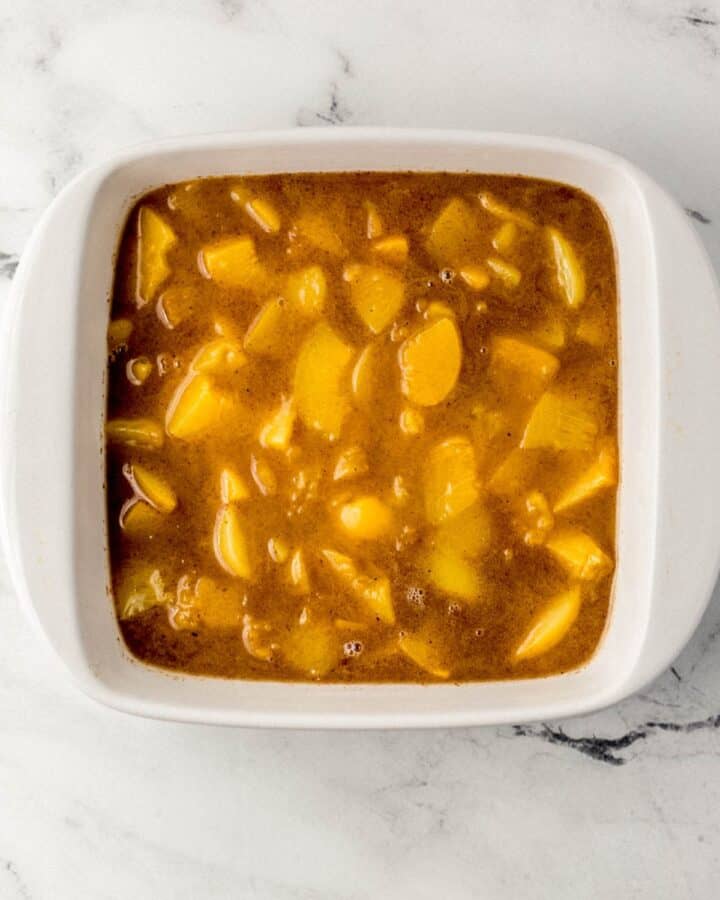 Peach mixture added to square white baking dish on marble surface. 