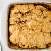 Close up overhead view of finished peach cobbler in square white baking dish.