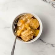 Overhead view of small bowl of peach cobbler with spoon in it.