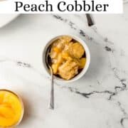 Bowl of peach cobbler with spoon in it on pin with text overlay.