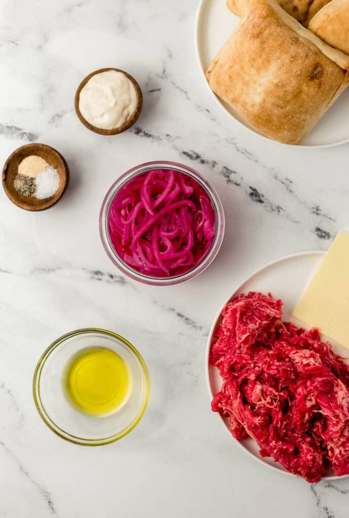 ingredients to make toasted steak sandwich on marble surface in separate bowls and plates