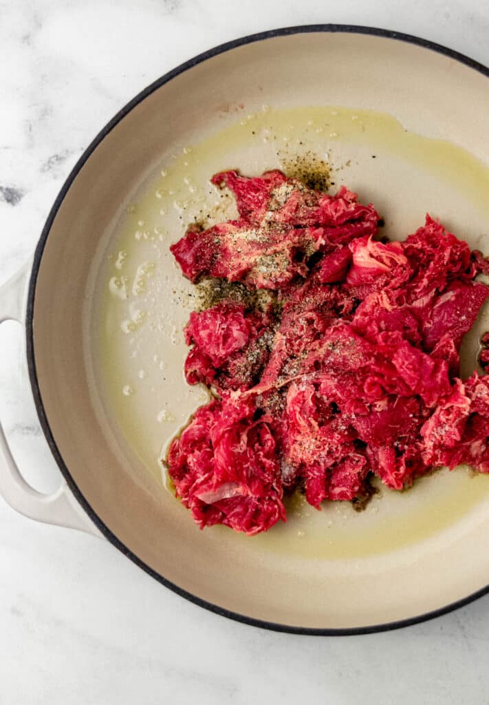 raw ribeye steak in white pan with seasoning and olive oil