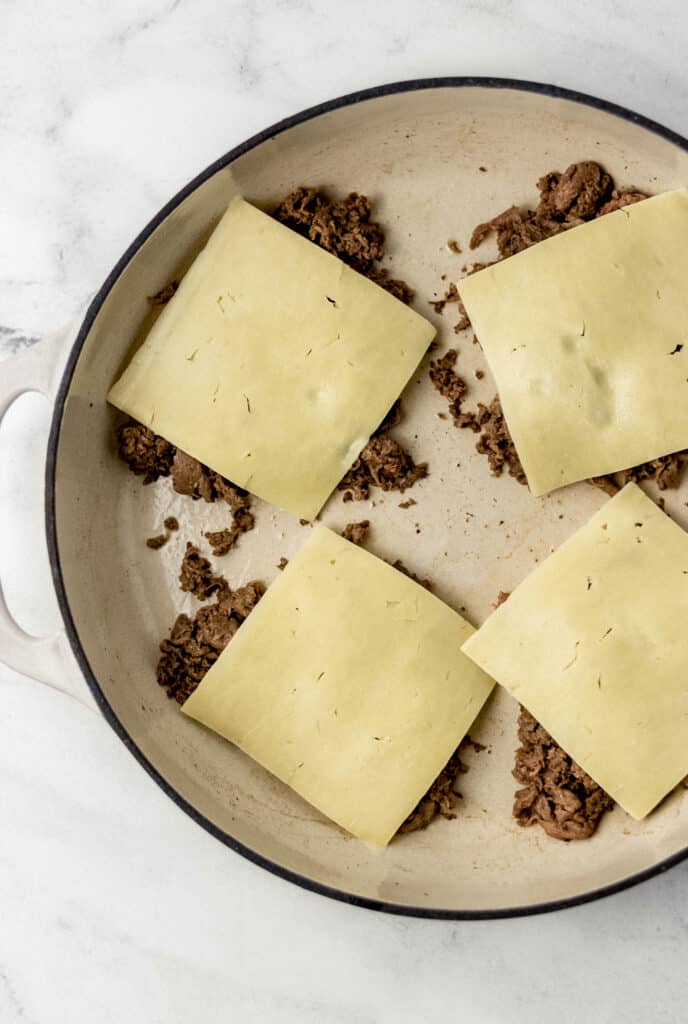 cooked steak topped with white cheddar cheese slices in pan 