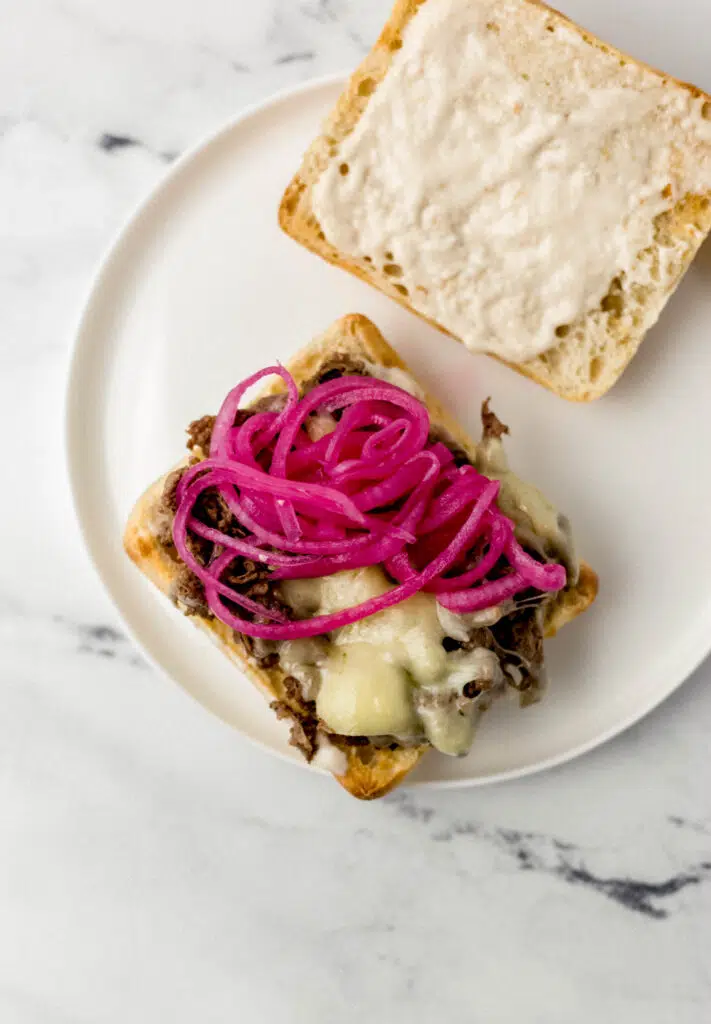 steak sandwich on white plate topped with pickled onions