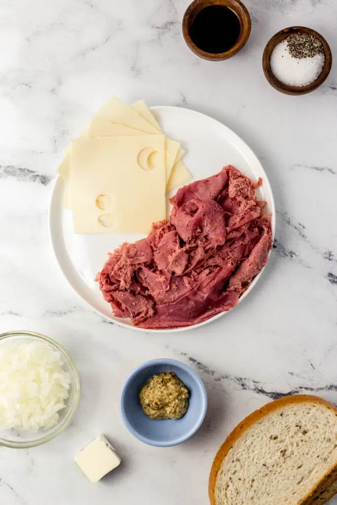 ingredients needed to make sandwich in separate small bowls and a plate on marble surface 