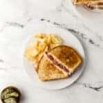 corned beef grilled cheese sandwiches on white plates with chips and pickles
