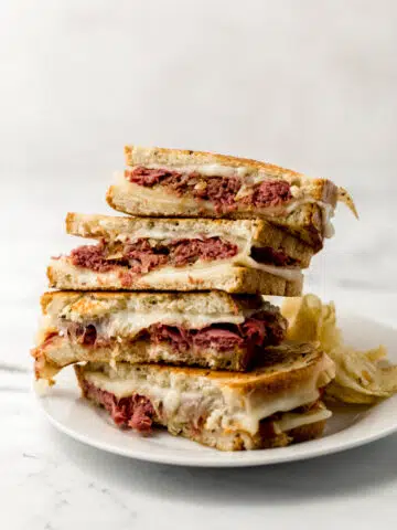 two grilled cheese sandwiches cut in half and stacked on white plate with chips