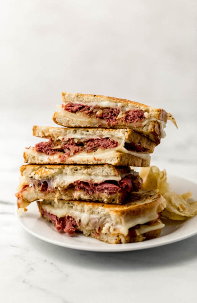 close up side view corned beef grilled cheese sandwiches cut in half on white plate with chips 
