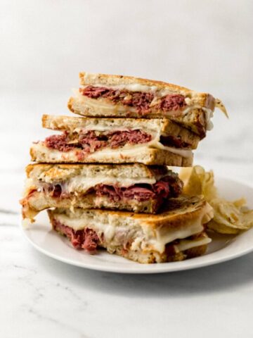 two grilled cheese sandwiches cut in half and stacked on white plate with chips