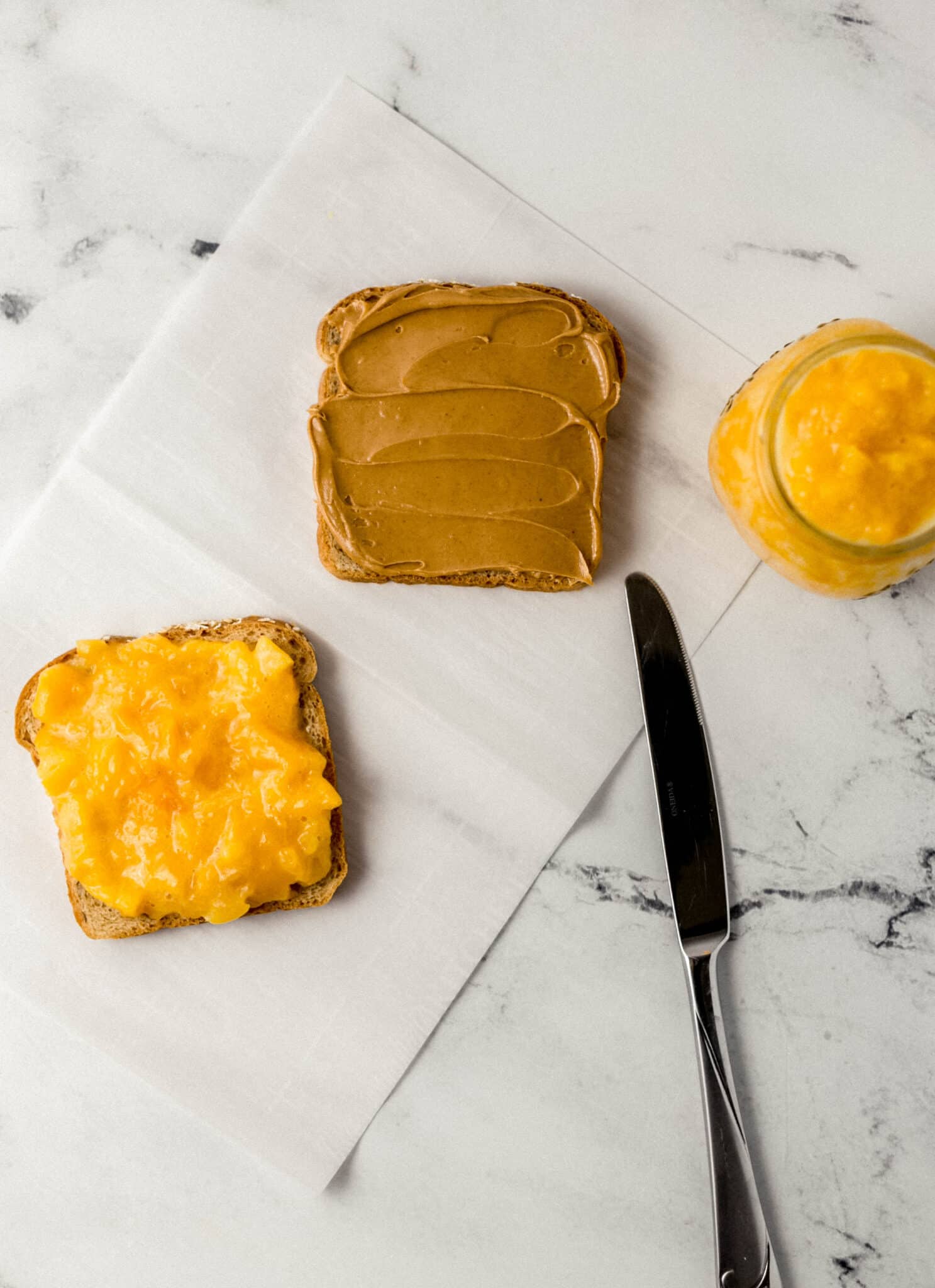 two slices of bread with jam and peanut butter beside knife and jar of jam