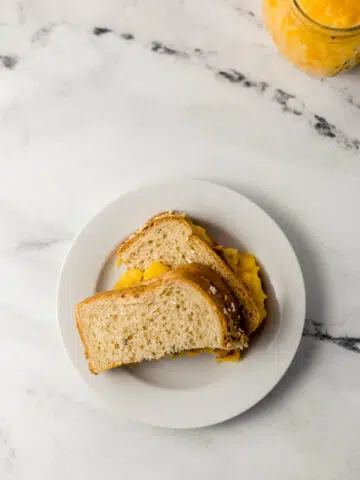 overhead view of sandwich cut in half on small white plate with jar of jam in the background