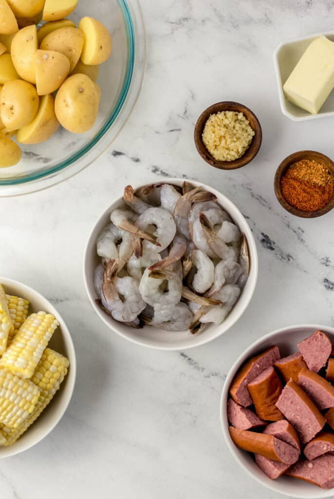ingredients needed to make sheet pan shrimp boil in separate bowls on marble surface 