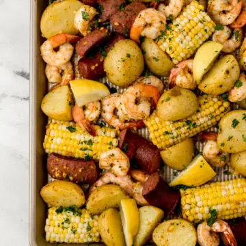 shrimp boil on sheet pan topped with chopped fresh parsley and lemon wedges