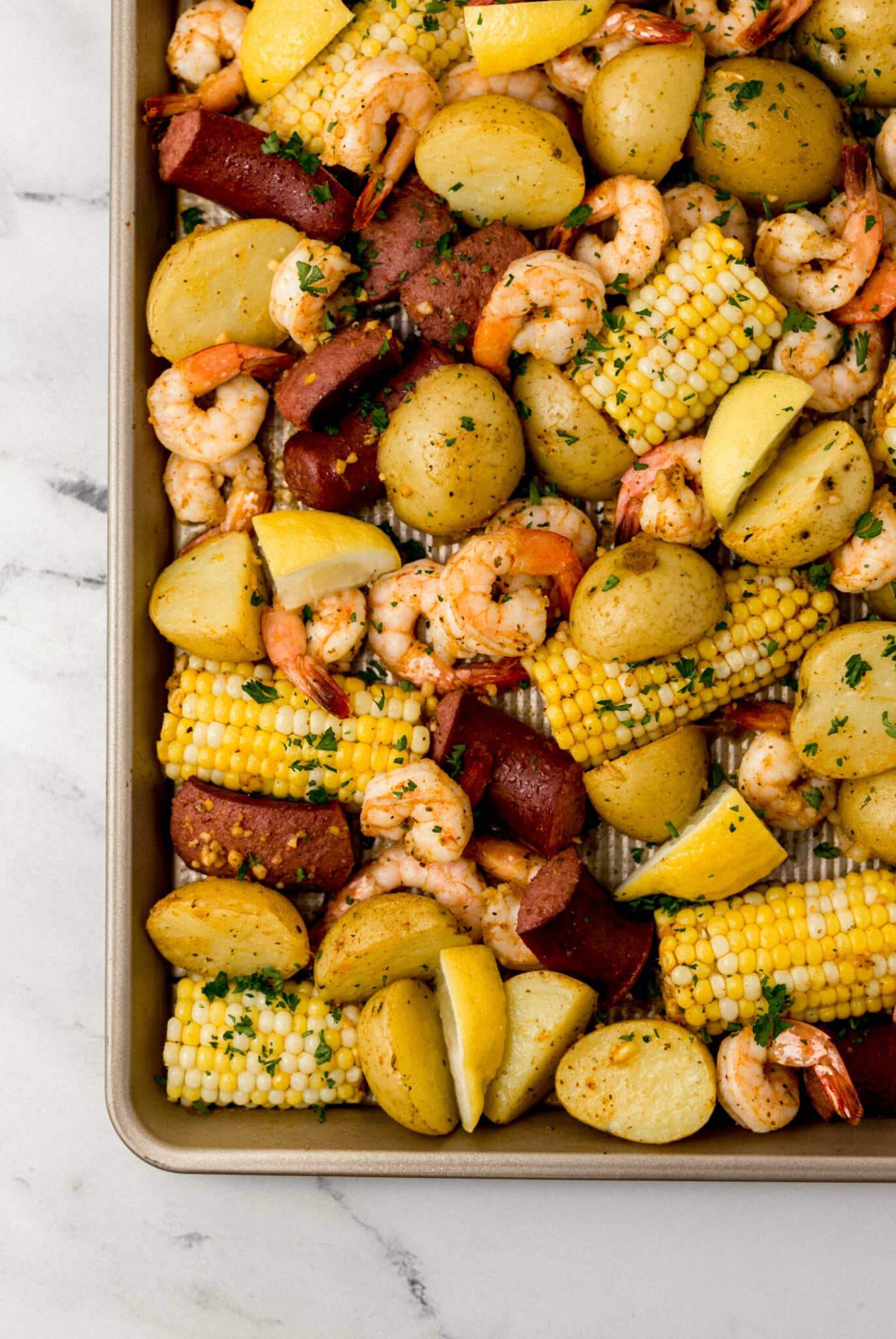 shrimp boil on sheet pan topped with chopped fresh parsley and lemon wedges