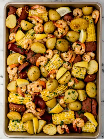 overhead view of shrimp boil on sheet pan topped with parsley and lemon wedges