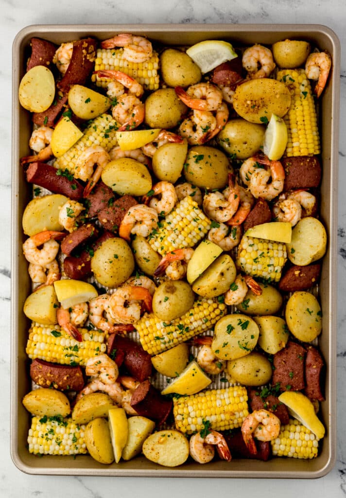 overhead view of finished shrimp boil on sheet pan topped with fresh parsley and lemon wedges